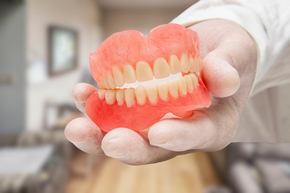 A gloved hand gently holds a set of pink and white dentures, showcasing a natural-looking smile replacement.