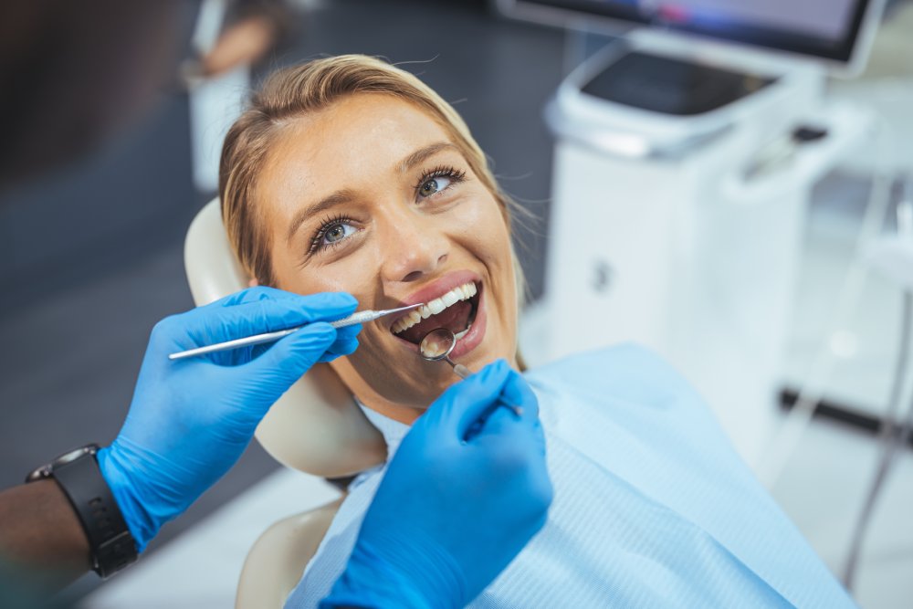 Perfect smile! Part of dentist examining his beautiful patient in dentist office. European young woman smiling while looking at mirror in dental clinic