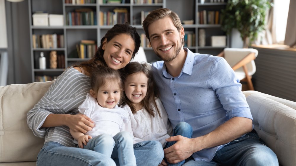 Smiling man in casual outfit standing on a city street – Ron Duffin DDS Portrait happy young family sitting on cozy couch in living room, smiling beautiful mother and father hugging two little daughters, looking at camera, posing for photo at home together