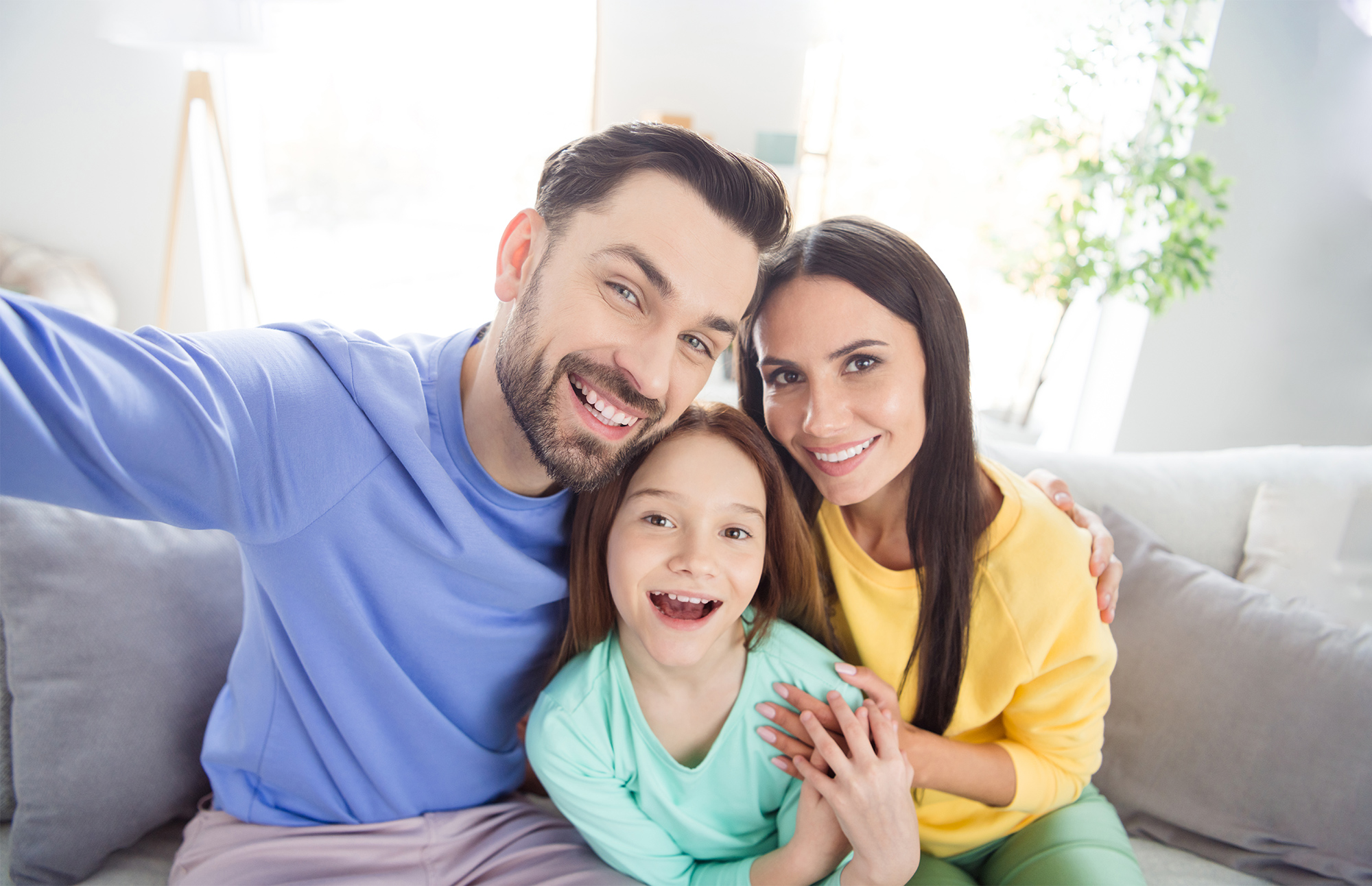 A smiling family sitting together on a couch taking a selfie, representing the confidence and happiness that comes from maintaining healthy smiles through professional dental care - Menifee dentist.